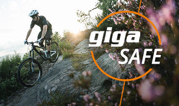 Ein Radfahrer mit Helm fährt mit seinem Mountainbike einen felsigen Pfad entlang, umgeben von Laub. Die Worte „giga SAFE“ sind in fettem, weißem und orangefarbenem Text darübergelegt.