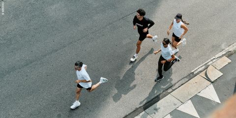 Vier Personen laufen gemeinsam auf einer gepflasterten Straße, von oben gesehen, in Sportkleidung und Turnschuhen.
