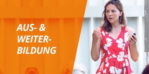 Eine Frau in einem rot-weißen Blumenkleid spricht und hält ein kleines Gerät in der Hand. Im Hintergrund ist eine orangefarbene Überlagerung mit den Worten „AUS- & WEITER-BILDUNG“ auf der linken Seite zu sehen.
